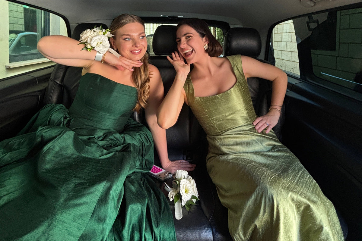 Two bridesmaids smiling in their bridesmaid dresses, sat in a car.
